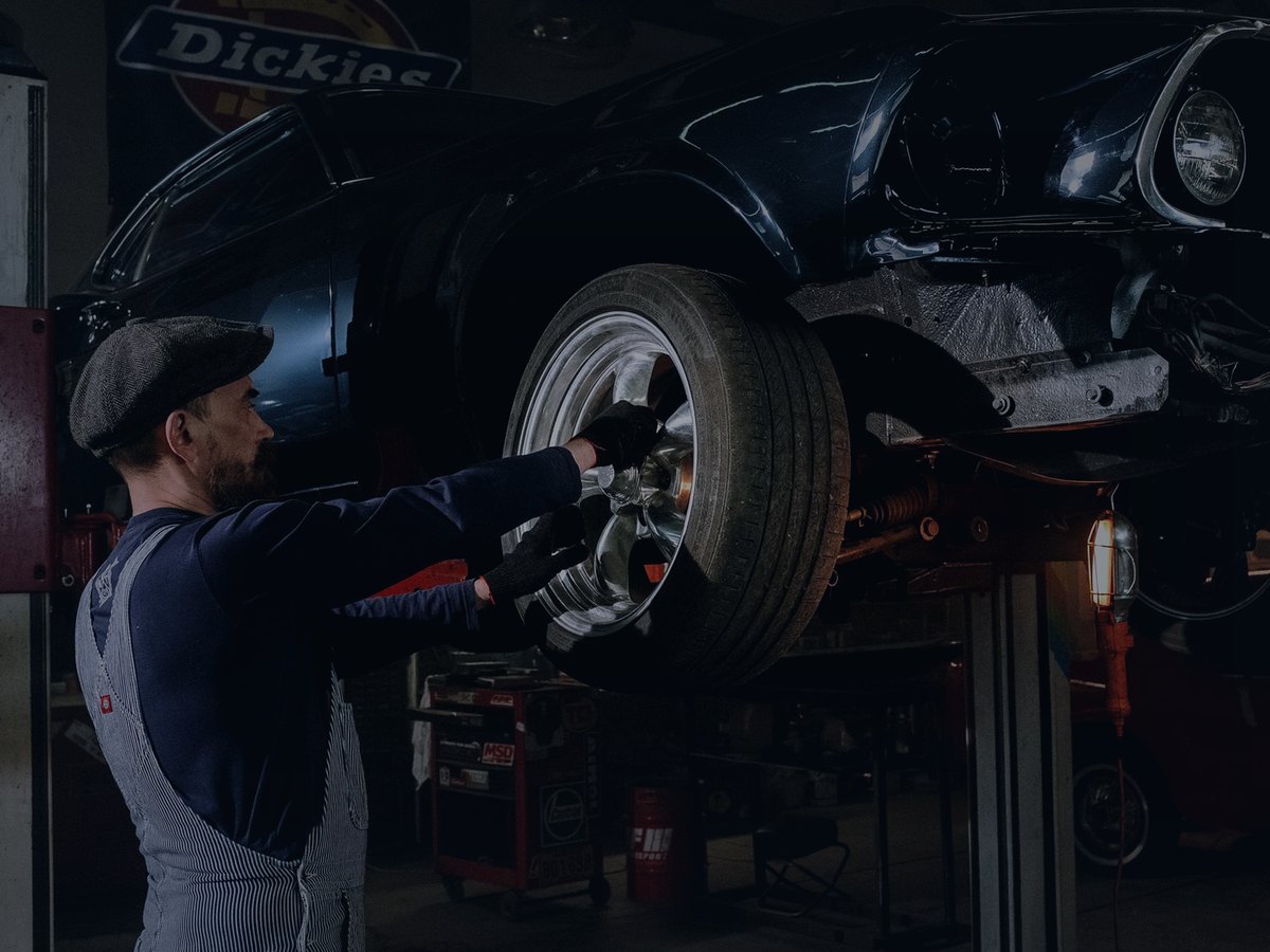 Car raised on a two-post lift while a mechanic works on the wheel